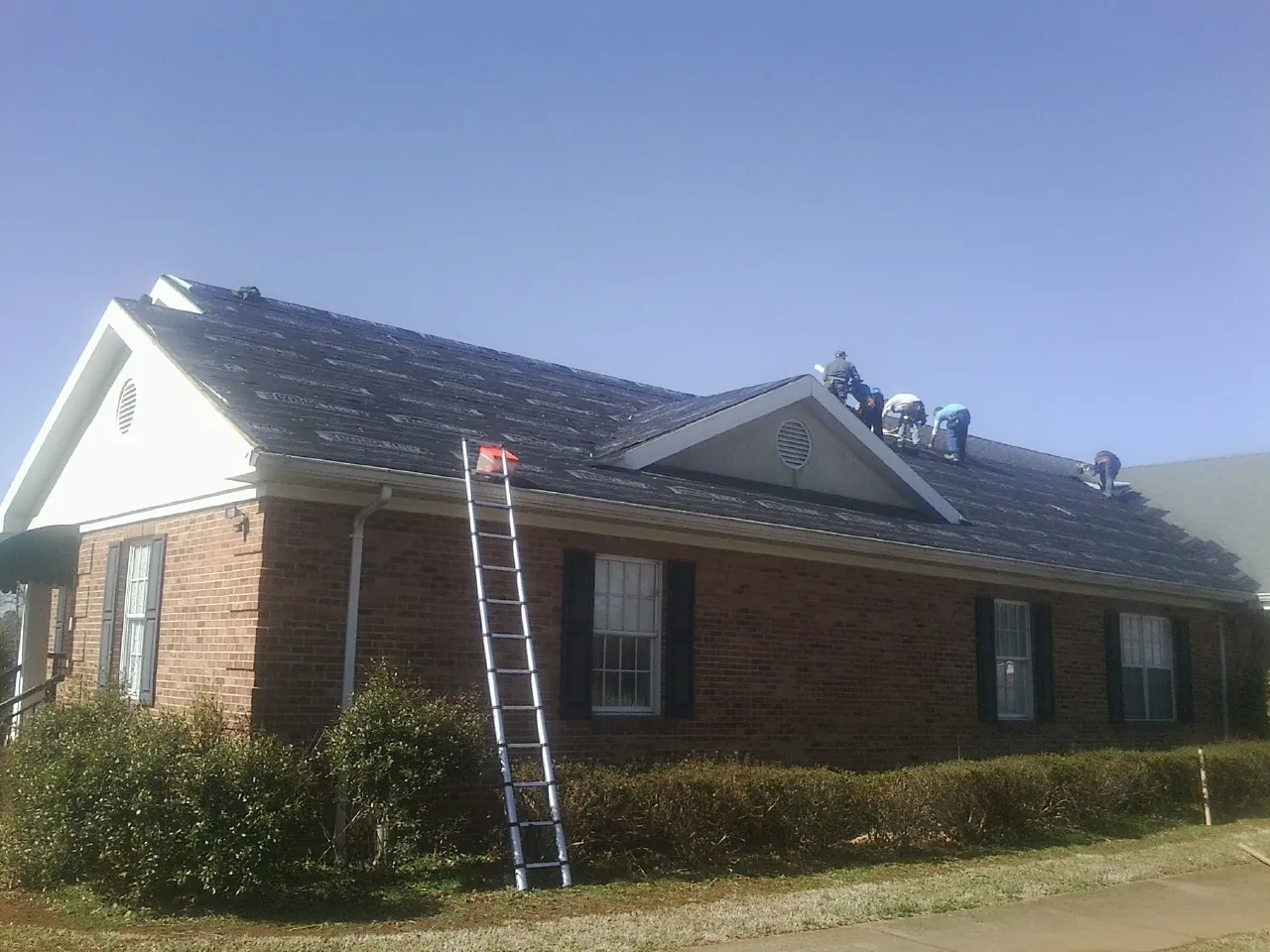 Crew tearing shingles off a brick ranch roof with a ladder set — Emergency Roof Repair work by our crew in Hightstown