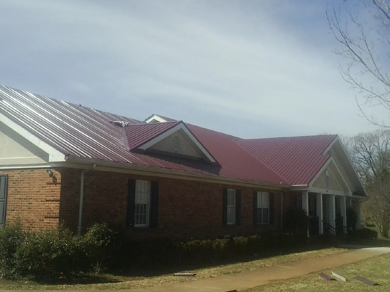 Red metal roof with gabled entries on a long brick building, from a Hail Damage Roof Repair job in Hightstown