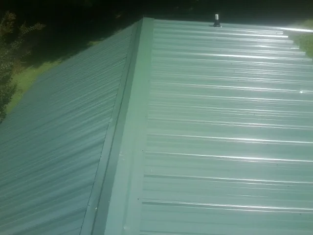New green metal panels meeting at the ridge of a roof — Flat Roof Repair work by our crew in Hightstown