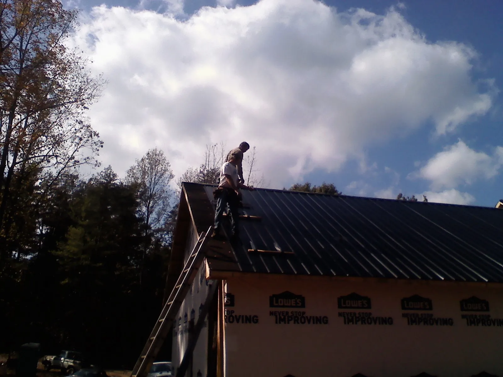 Roofer fastening dark metal panels high against a cloudy sky, from a Roof Inspection job in Hightstown