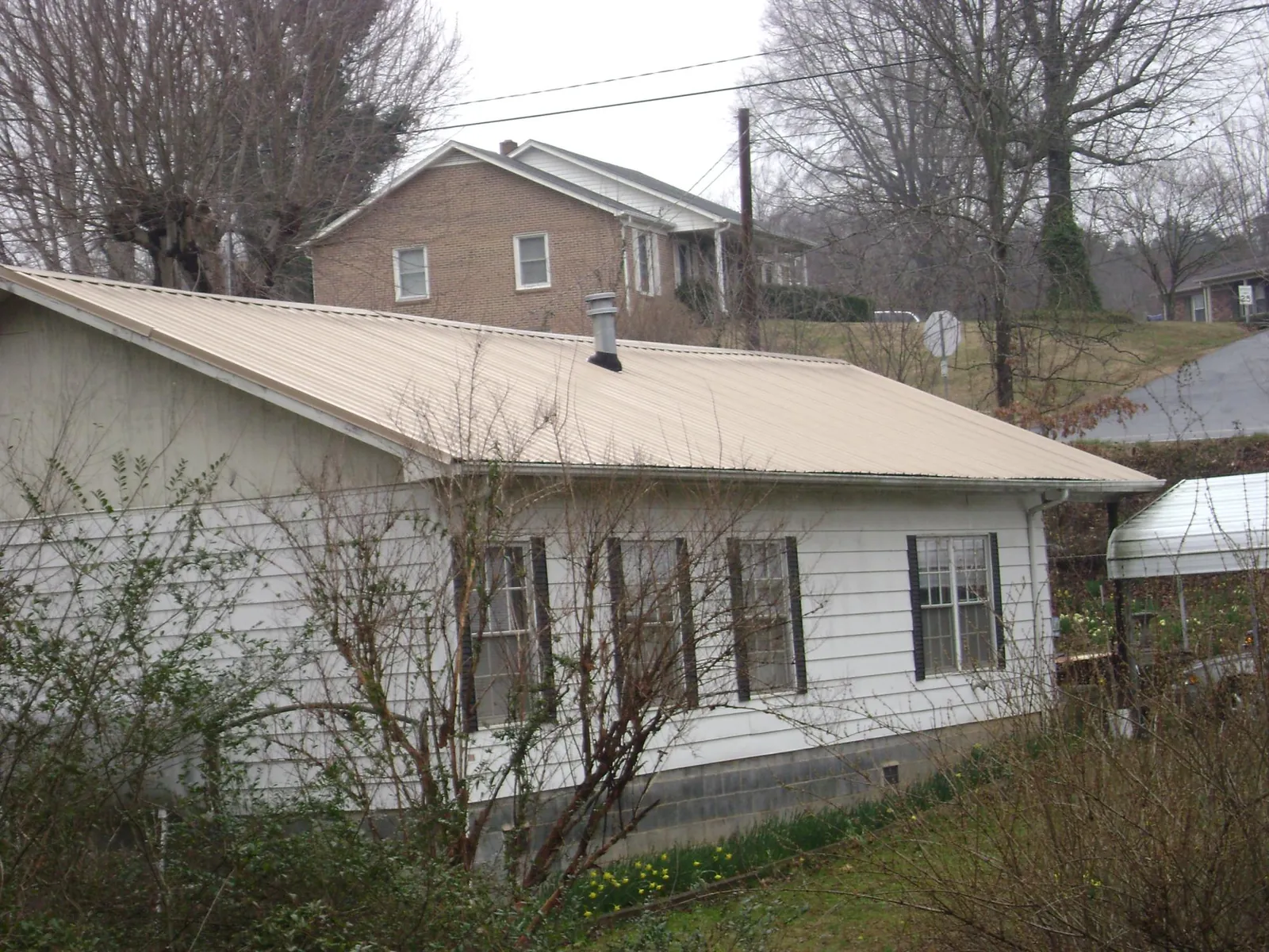 Tan metal roof on a white sided house set into a hillside — Commercial Roofing by Roofing Brothers in Hightstown